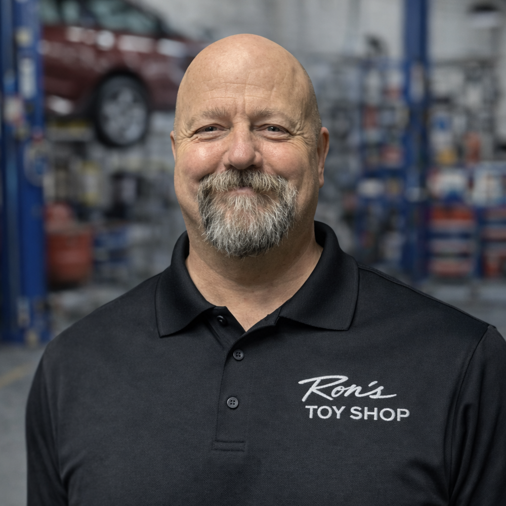 Man wearing a black shirt with 'Ron's Toy Shop' logo in a workshop setting
