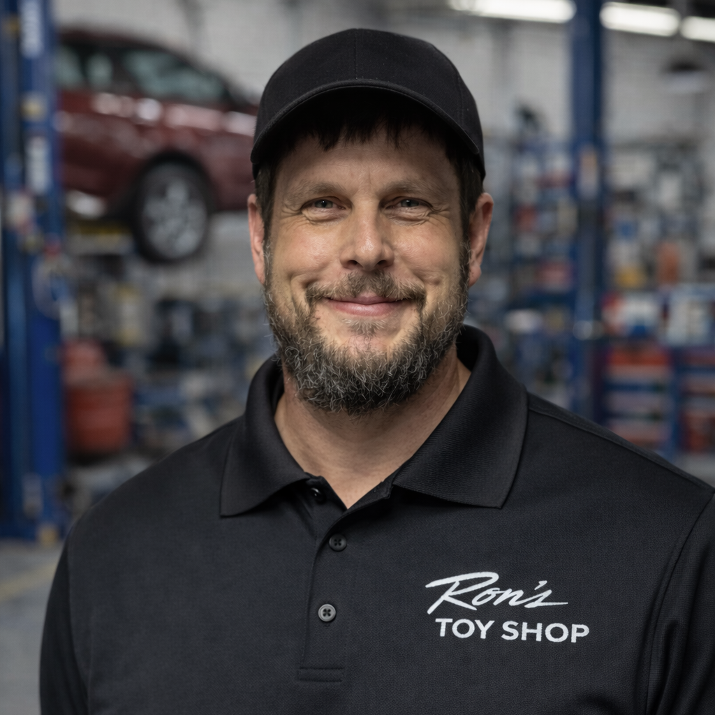 Man wearing a black shirt with 'Ron's Toy Shop' logo in a workshop setting