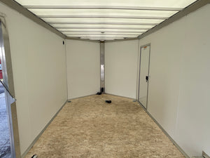 The inside of a large trailer or cargo space with off-white panel walls, a light wood composite floor, and a metal door frame on the right side.