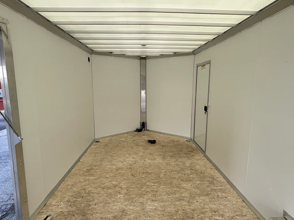 The inside of a large trailer or cargo space with off-white panel walls, a light wood composite floor, and a metal door frame on the right side.
