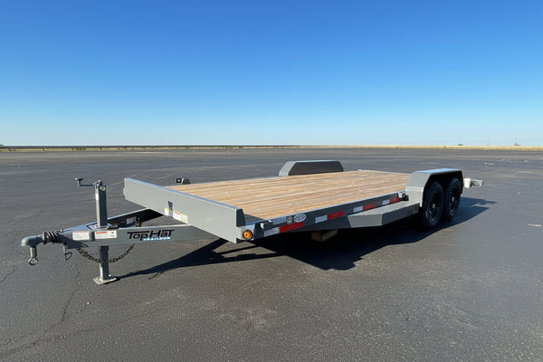 A low-profile tandem flatbed trailer with a wood deck and gray metal frame, parked on asphalt in an outdoor dealership lot.
