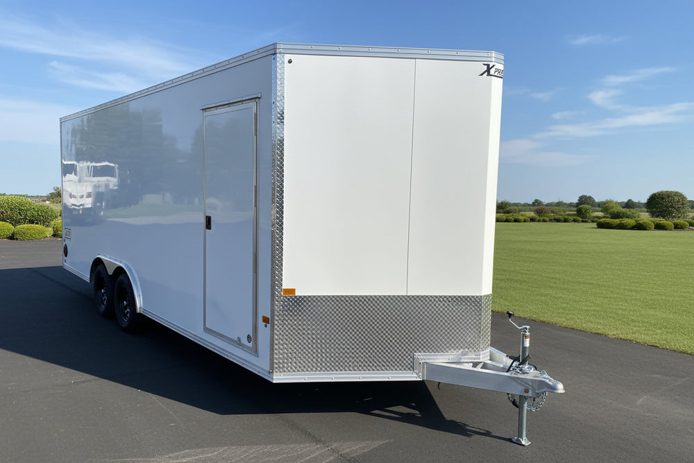 A white enclosed cargo trailer parked outdoors on a paved lot next to a red building. The trailer has a side door, a diamond-plate lower section, dual wheels, and a hitch at the front.